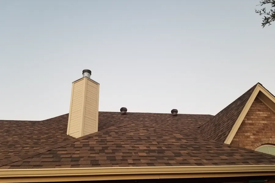 Chimney rising from brown shingles under a pale sky