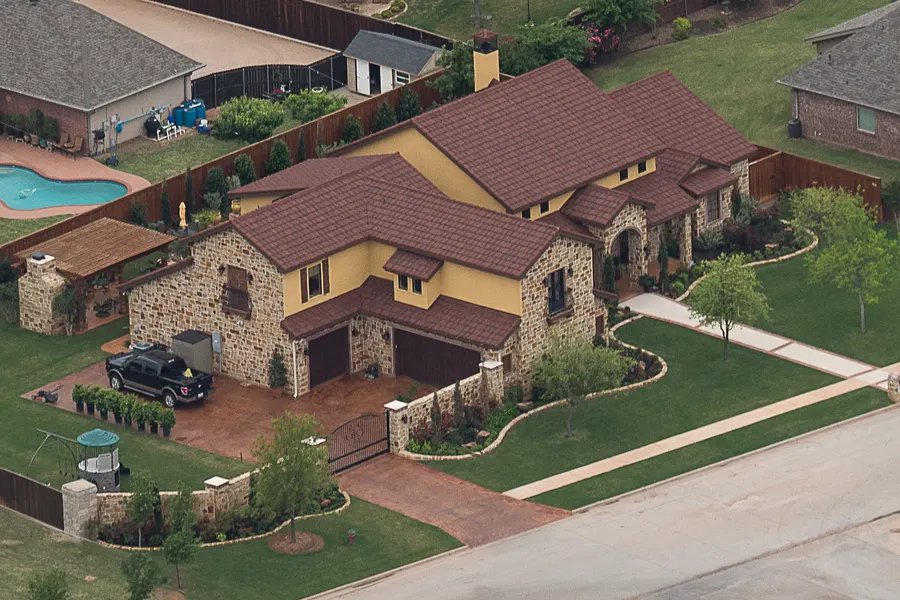 Stone and stucco house with a dark red-brown roof, seen from above