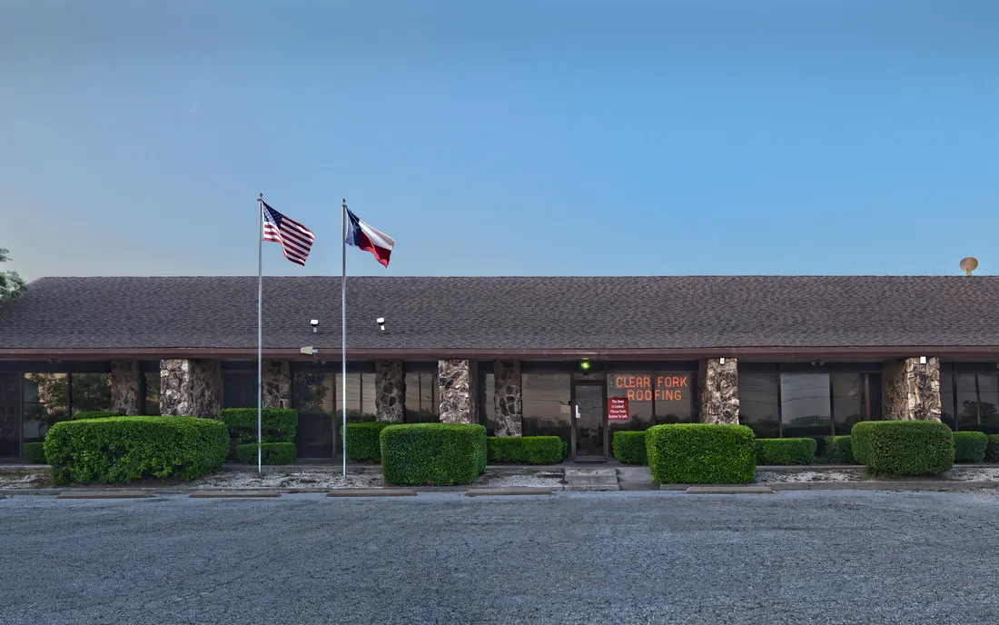 The Clear Fork Roofing office, a low stone-front building with an American flag and a Texas flag out front